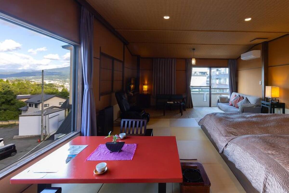 A hotel room with a bed, a desk, a chair, a sofa, and a view of the city.
