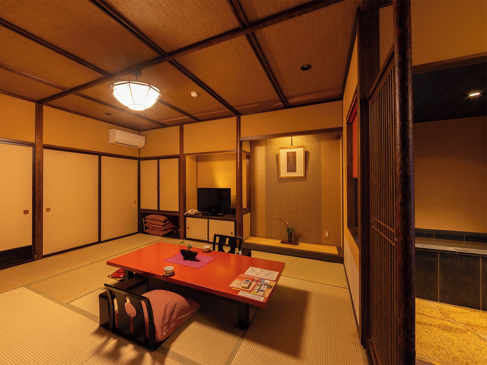 Una habitación japonesa tradicional con suelo de tatami, una mesa baja con cojines, un televisor y una puerta corredera.