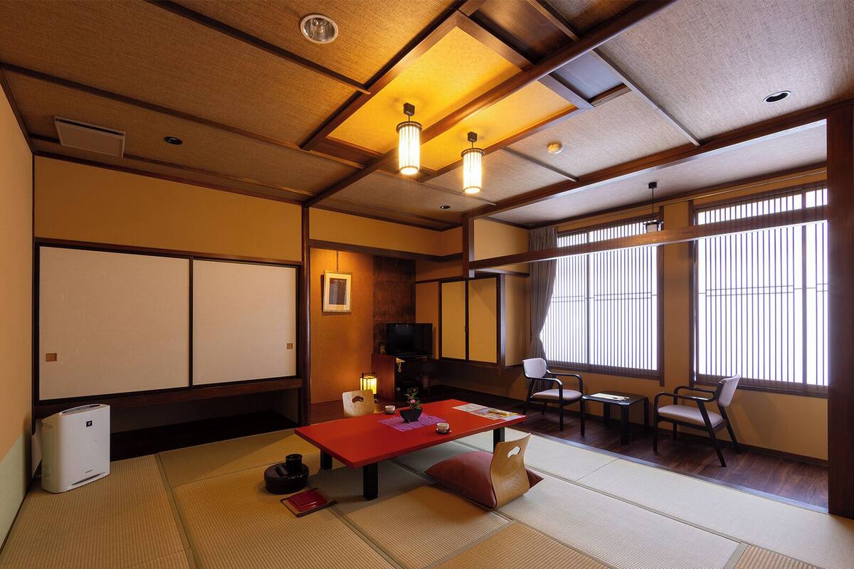 A traditional Japanese room with tatami flooring, a low table with cushions, a television, and sliding doors.