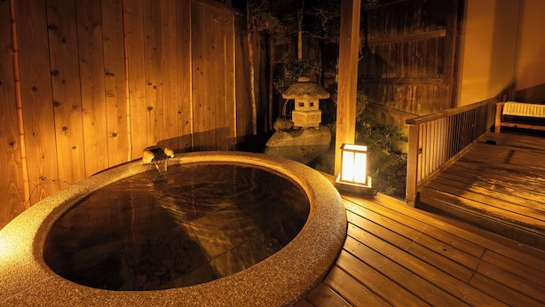 Una terraza de madera con un baño de aguas termales, un farol y un candelabro de piedra.