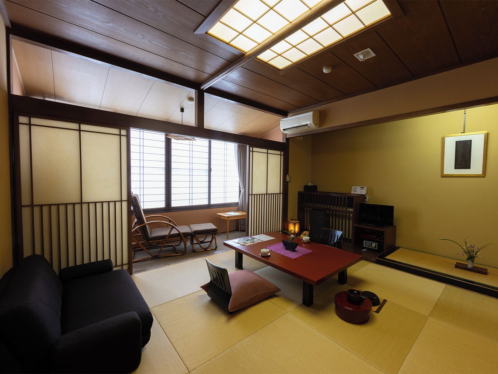 Una habitación tradicional japonesa con suelo de tatami, una mesa baja, un sofá y un puertas correderas.