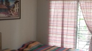 Una habitación con dos camas, cada una con ropa de cama a rayas de colores, un cuadro en la pared y una ventana con cortinas a rayas.