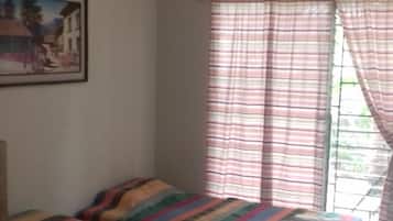 A room with two beds, each with colorful striped bedding, a painting on the wall, and a window with striped curtains.
