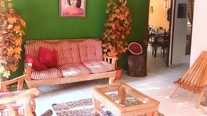 Sala de estar con una pared verde, un sofá a rayas, un ventilador de techo y una zona de comedor visible a través de una puerta abierta.