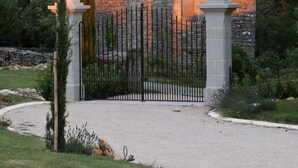 Una casa de piedra con techo de tejas, rodeada por un camino de grava y una valla de metal.