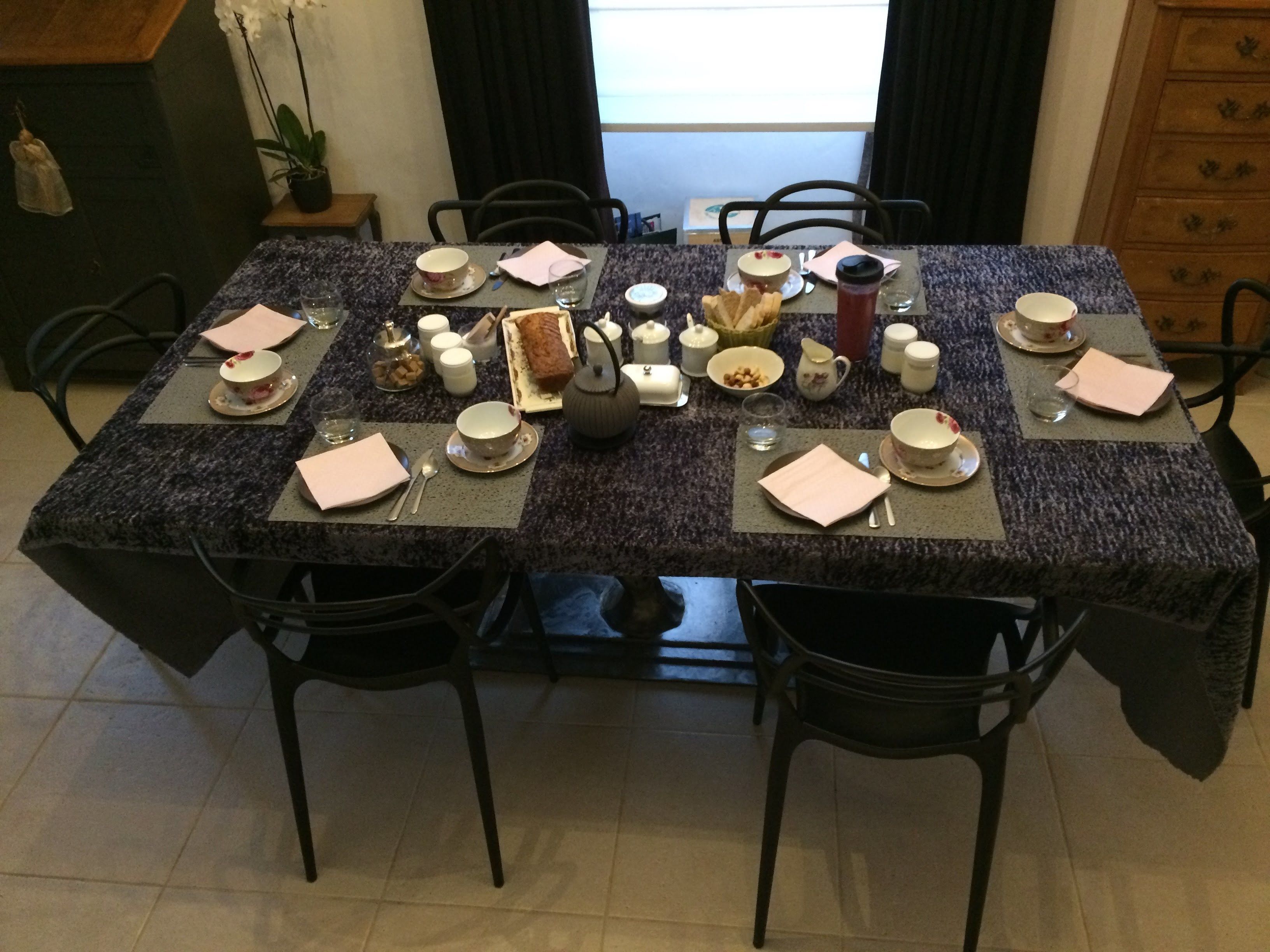 Une table à manger dressée avec des assiettes, des bols, des tasses et une théière, entourée de chaises.
