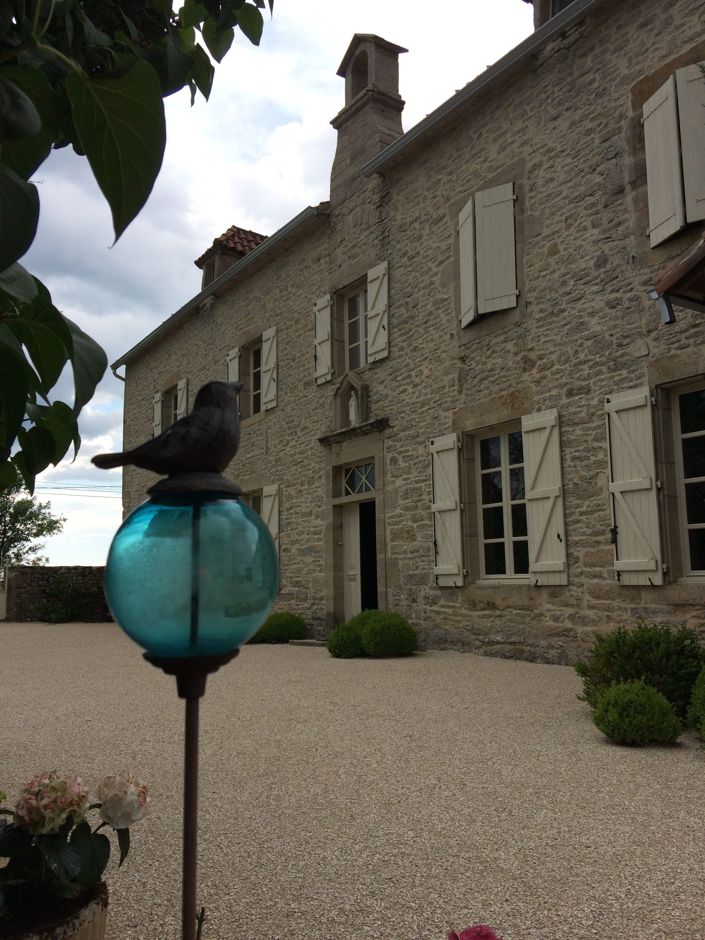 A stone building with shutters and a bird perched on a blue spherical object.