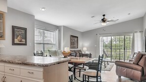 A spacious kitchen with a marble countertop, dining area with chairs, a sofa, and large windows with blinds. - Gorgeous Greens 2 Bedroom Condo by RedAwning (Branson)