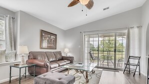 A modern living room with a leather sofa, glass coffee table, and a view of a balcony. - Gorgeous Greens 2 Bedroom Condo by RedAwning (Branson)