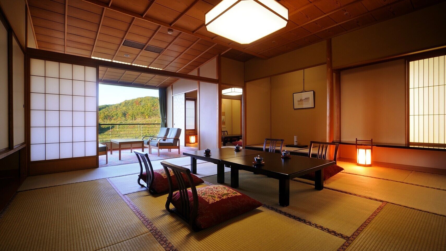 Ein traditioneller japanischer Raum mit Tatami-Böden, einem niedrigen Tisch mit Stühlen, Blick auf eine grüne Landschaft und einer hängenden Laterne.