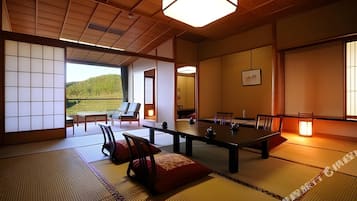A traditional Japanese room with tatami flooring, a low table, chairs, and a view of a hillside.