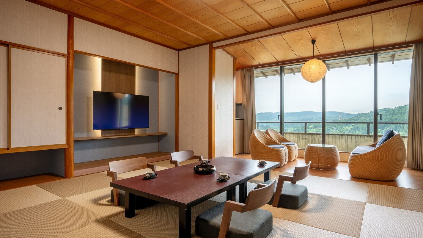 Ein traditioneller japanischer Raum mit Tatami-Bodenbelag, einem niedrigen Holztisch und einem an der Wand befestigten Fernseher.