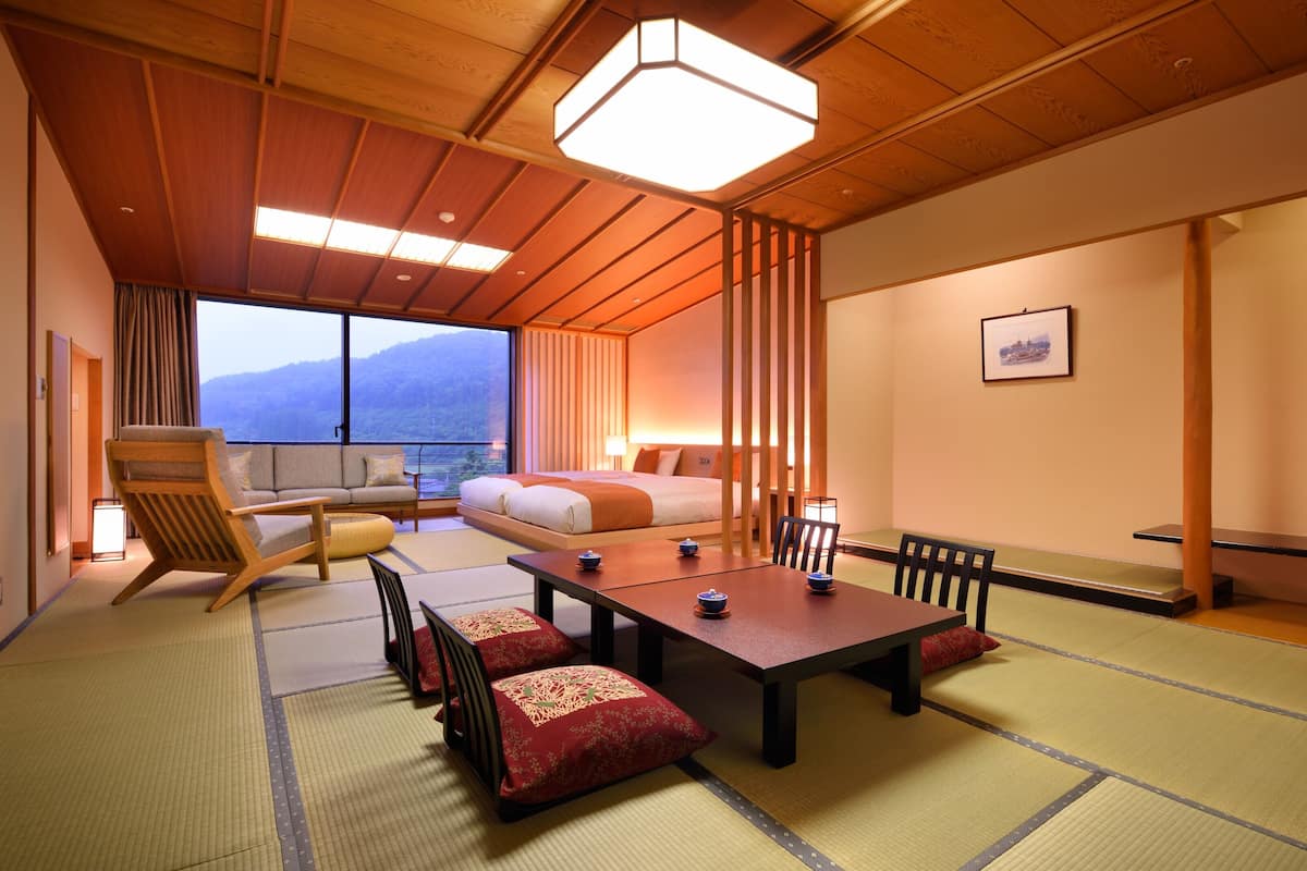 Ein traditioneller japanischer Raum mit Tatami-Boden, einem niedrigen Tisch mit Kissen, einer Couch und einem Bett mit Bergblick.