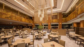 A spacious hotel lobby with multiple dining areas, a central bar, and a high ceiling with hanging lights. - Hotel Zuiho (Sendai)