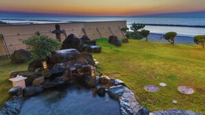 Un entorno sereno al aire libre con un jacuzzi de piedra, una valla de madera y vistas al océano al atardecer.
