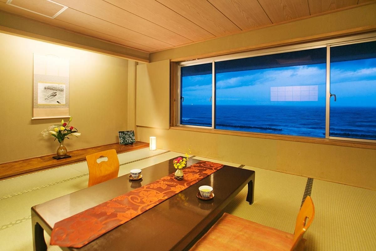 A traditional Japanese-style room with tatami flooring, a low table with a decorative runner, and a view of the ocean through a large window.