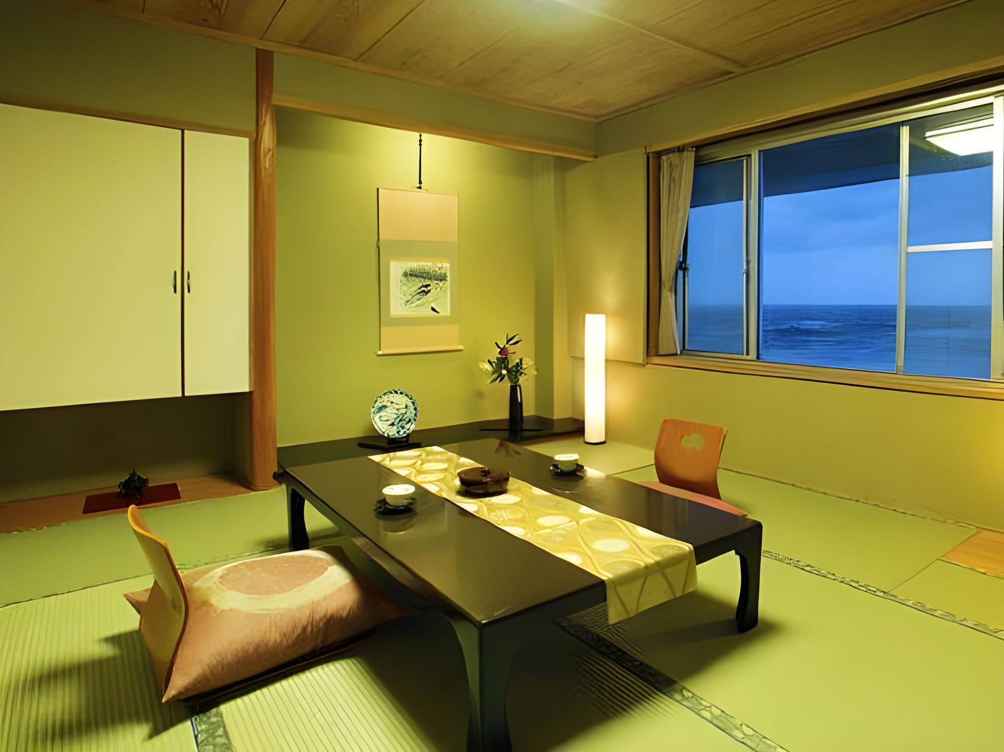 A traditional Japanese room with tatami flooring, a low table, a window with a view of the sea, and a sliding door.