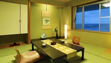 A traditional Japanese room with tatami flooring, a low table, a window with a view of the sea, and a sliding door.