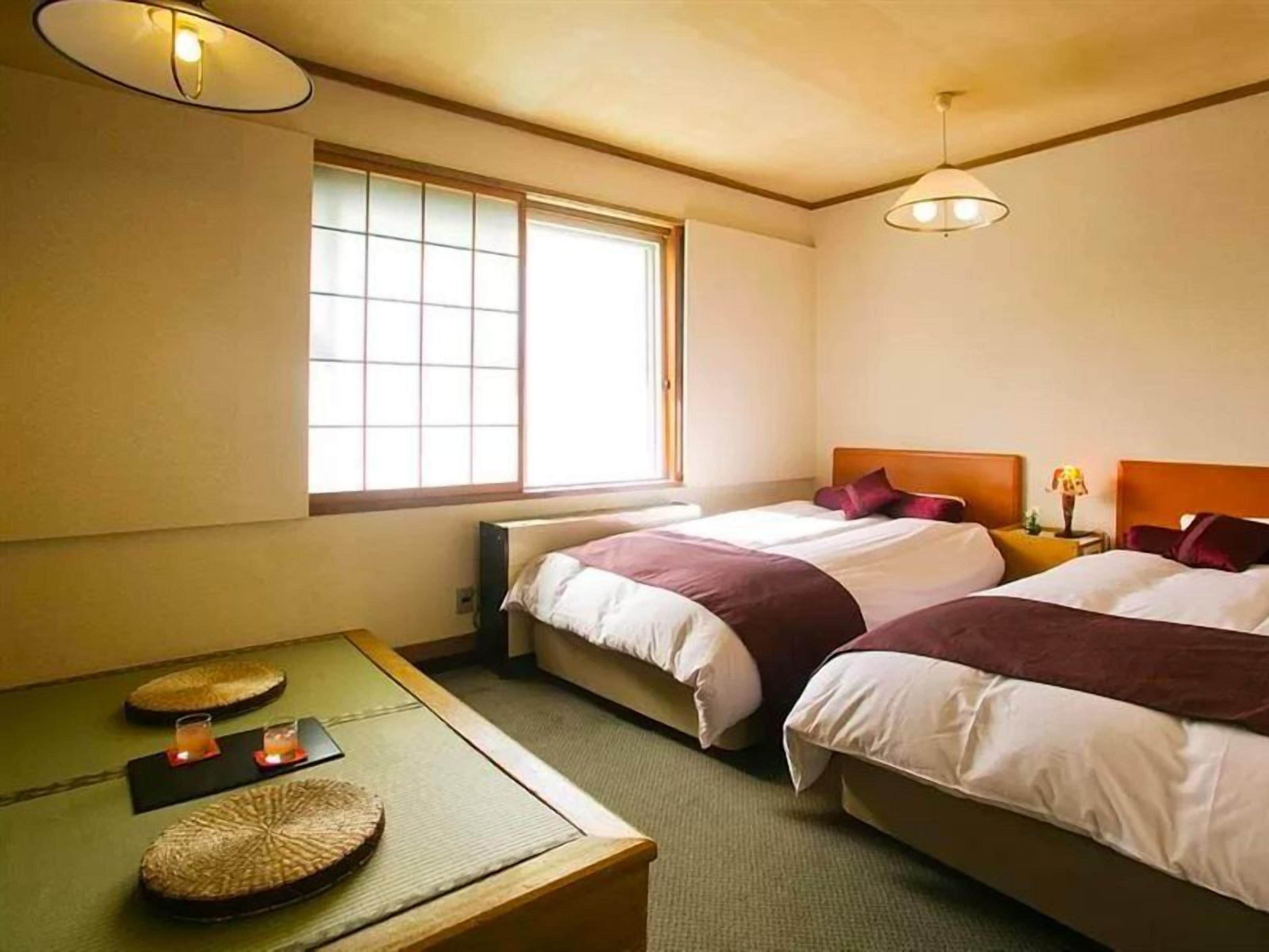 Una habitación de hotel con dos camas, una mesita con velas y una ventana con persianas.
