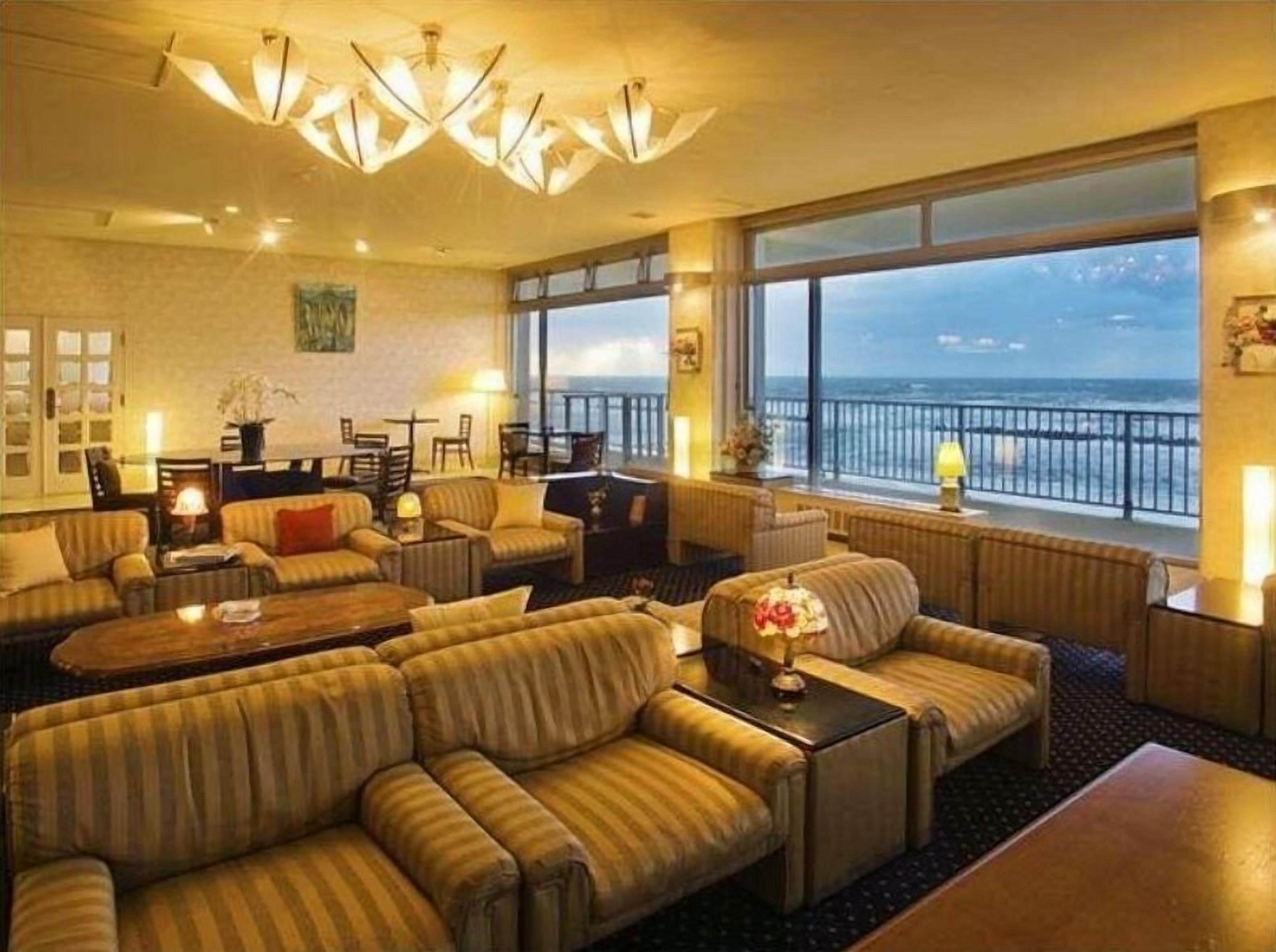 A spacious living room with multiple seating areas, large windows with a view, and a modern chandelier.