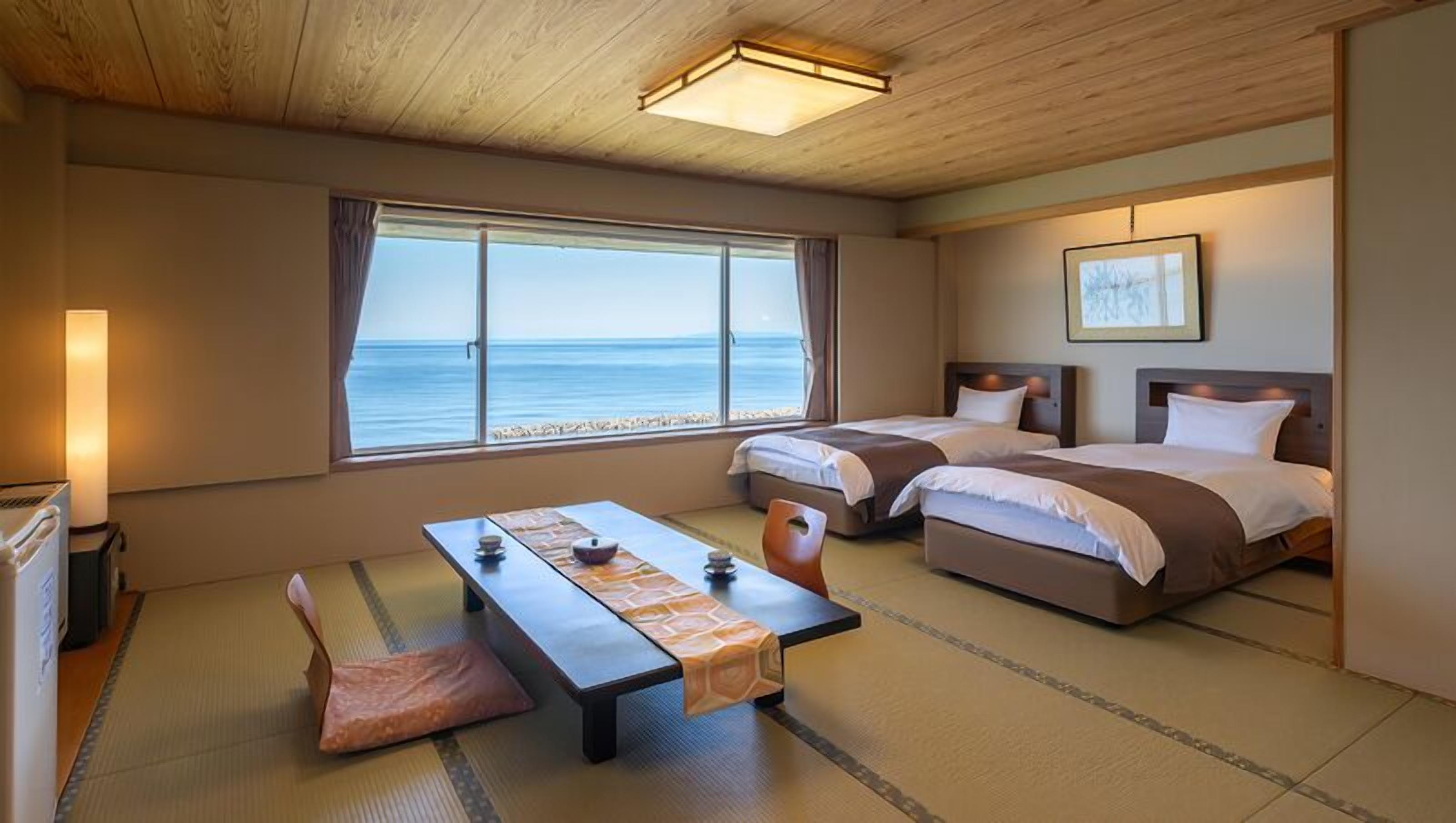 Una habitación con dos camas, una mesa y vista al mar.