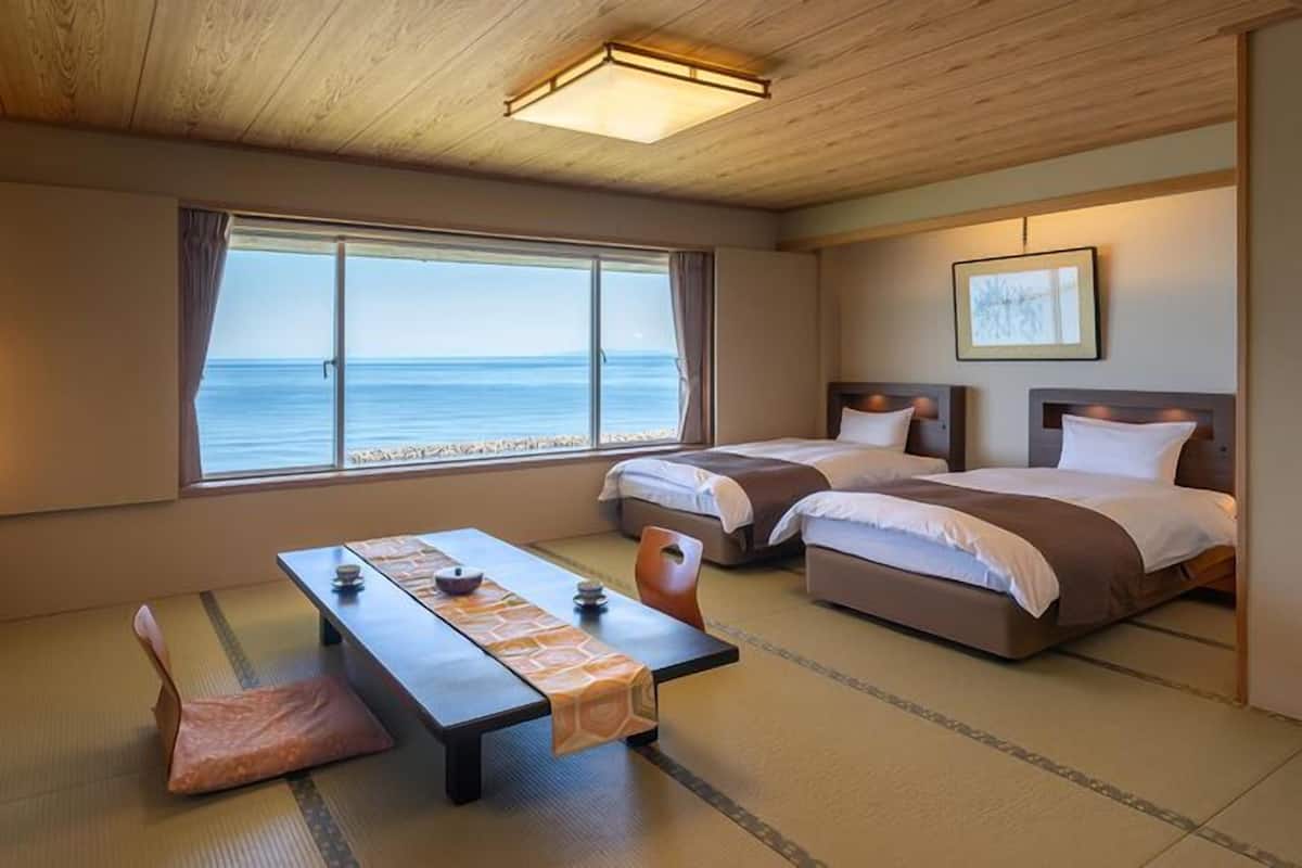 Una habitación con dos camas, una mesa y vista al mar.