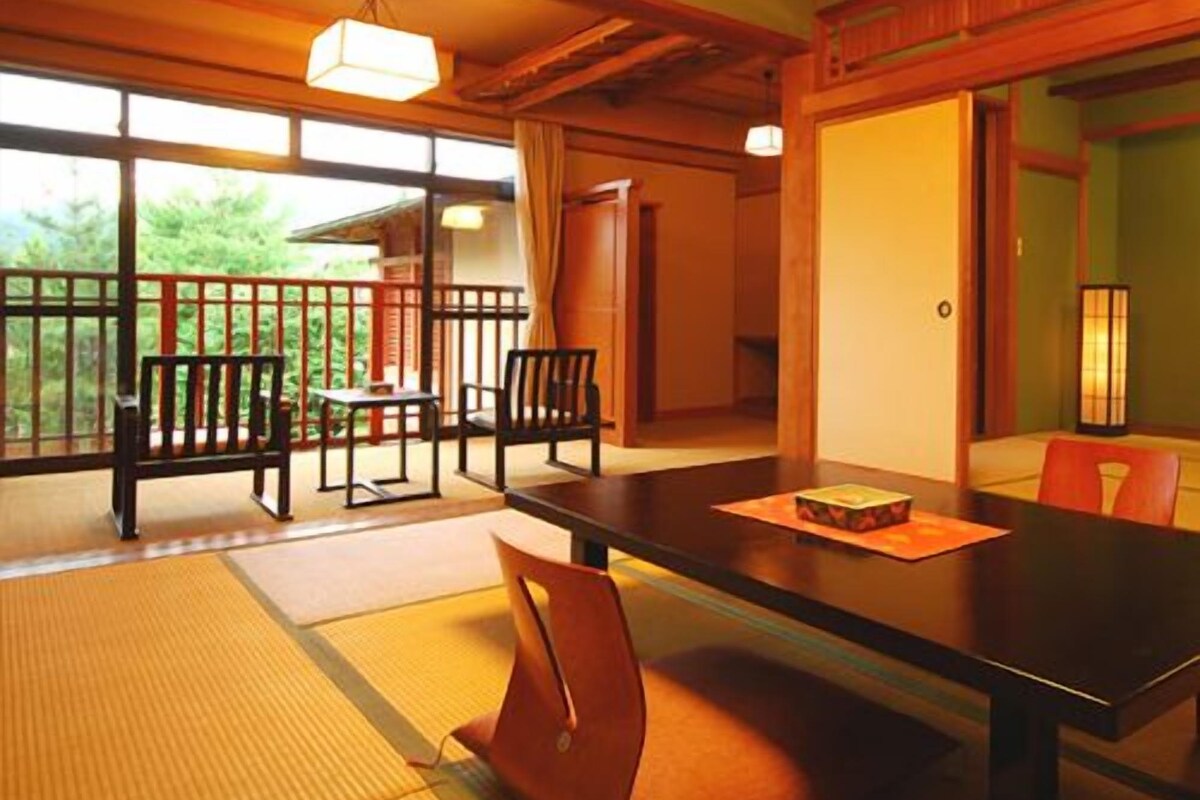 A traditional Japanese room with tatami flooring, a low table, and a view of greenery outside.