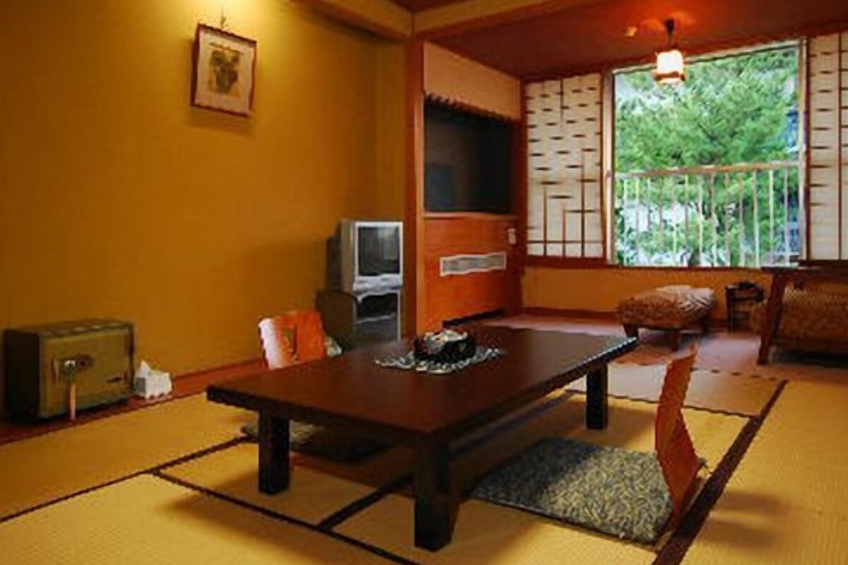 A traditional Japanese room with tatami flooring, a low table, a television, and a sliding door.