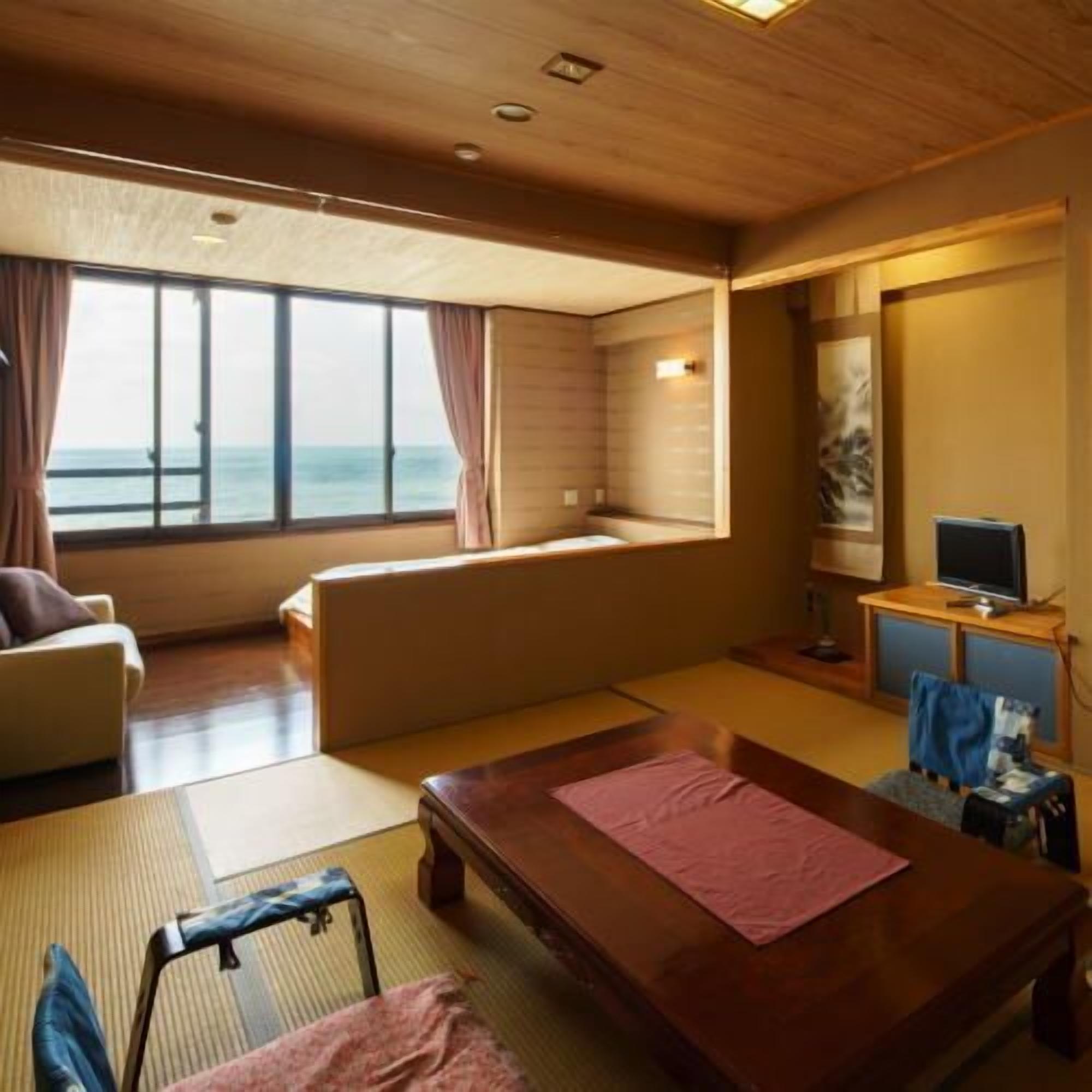 A room with a large window, a sofa, a wooden table, a TV, and a small seating area.
