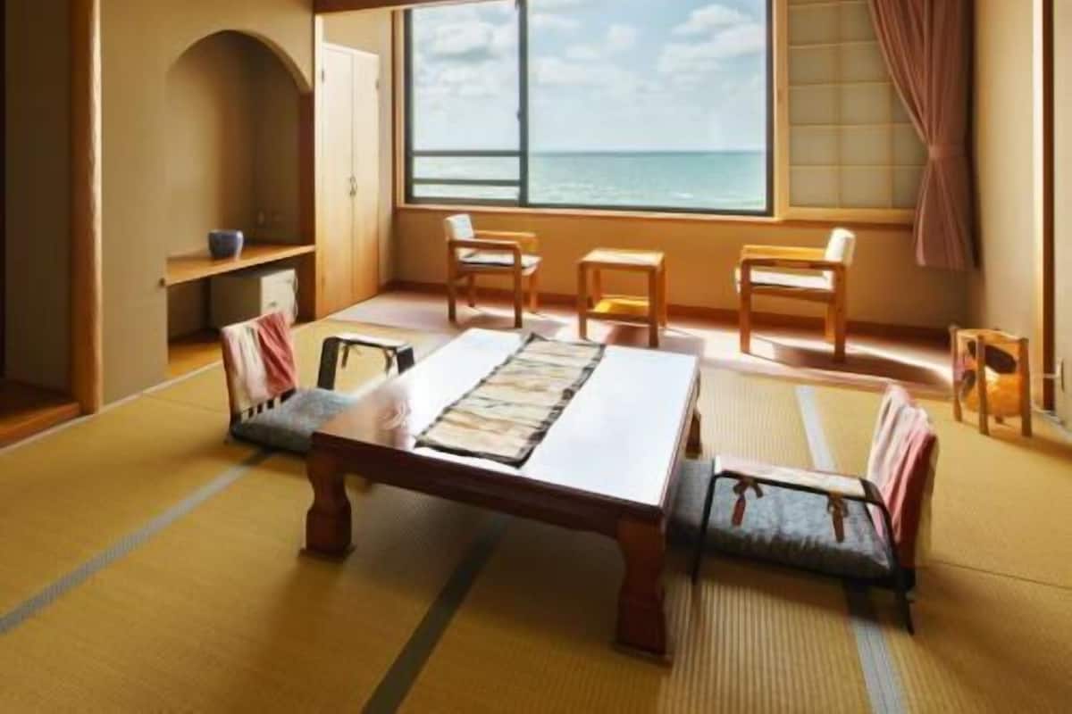 Una habitación japonesa tradicional con suelo de tatami, una mesa baja y vista al mar.