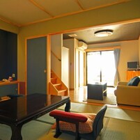 Una habitación con un futón de tatami, una mesa baja, un sofá y una escalera que lleva a otra habitación.
