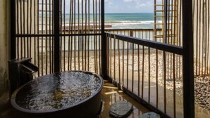 Ett rum vid stranden med ett stort stenfat, ett metallräcke och utsikt över havet.