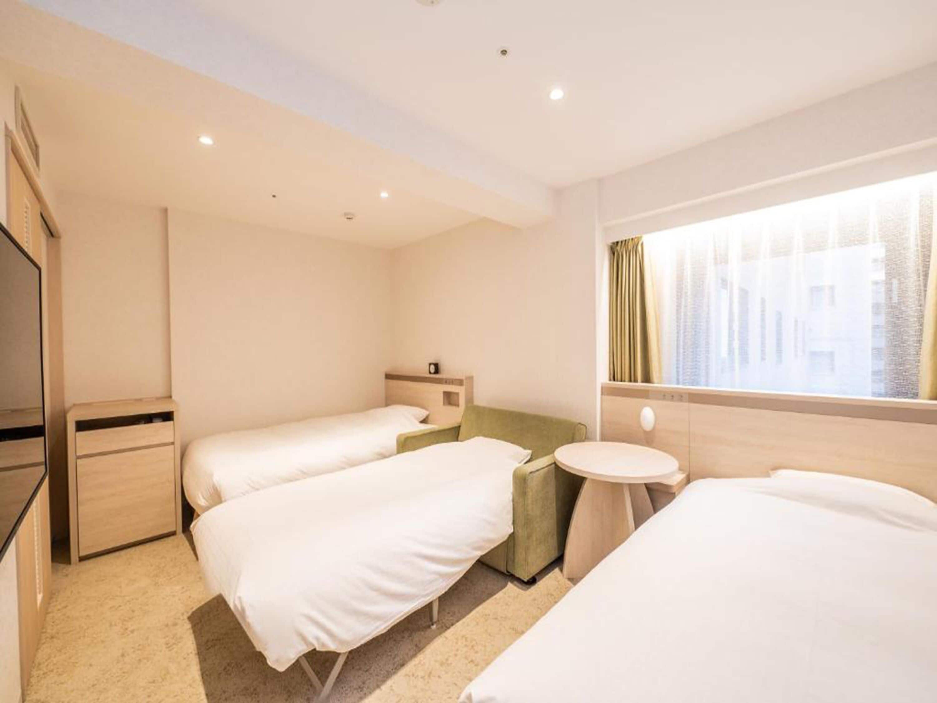 A hotel room with two single beds, a small round table, a nightstand, a mirror, and a window with curtains.