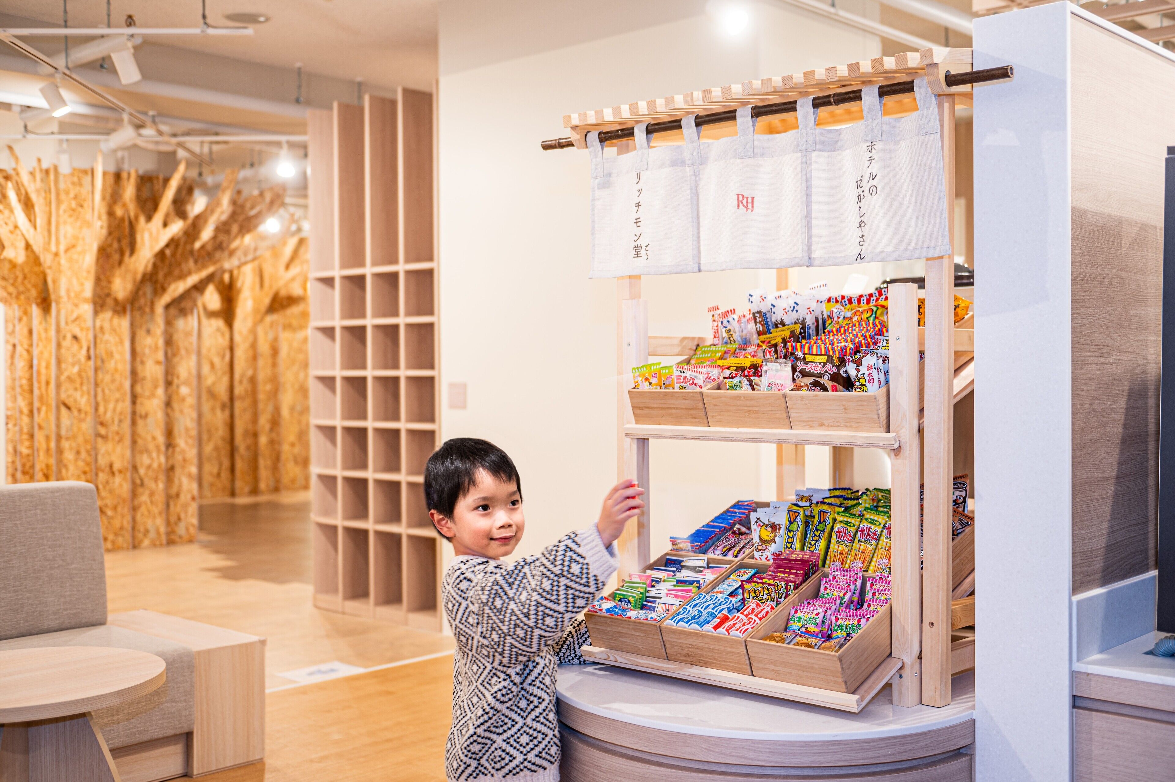 Et barn interagerer med en træstander med snacks i et moderne, godt oplyst butiksmiljø med trædetaljer og et minimalistisk design.