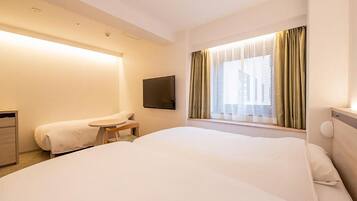 Habitación de hotel con una cama grande, una mesita pequeña, un televisor montado en la pared y un ventanal con cortinas.
