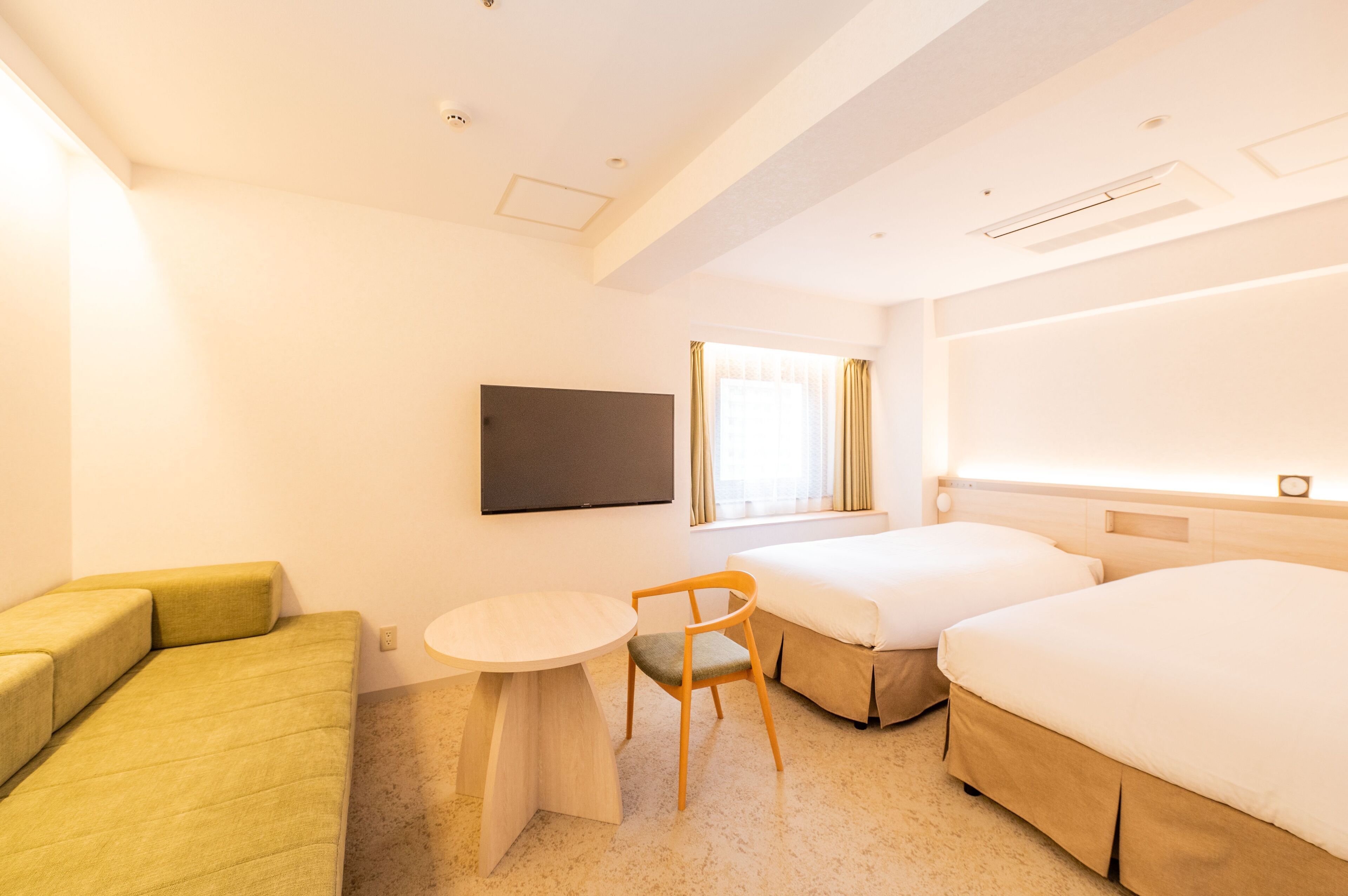 Habitación de hotel con sofá, una mesita, una silla, dos camas y televisión.