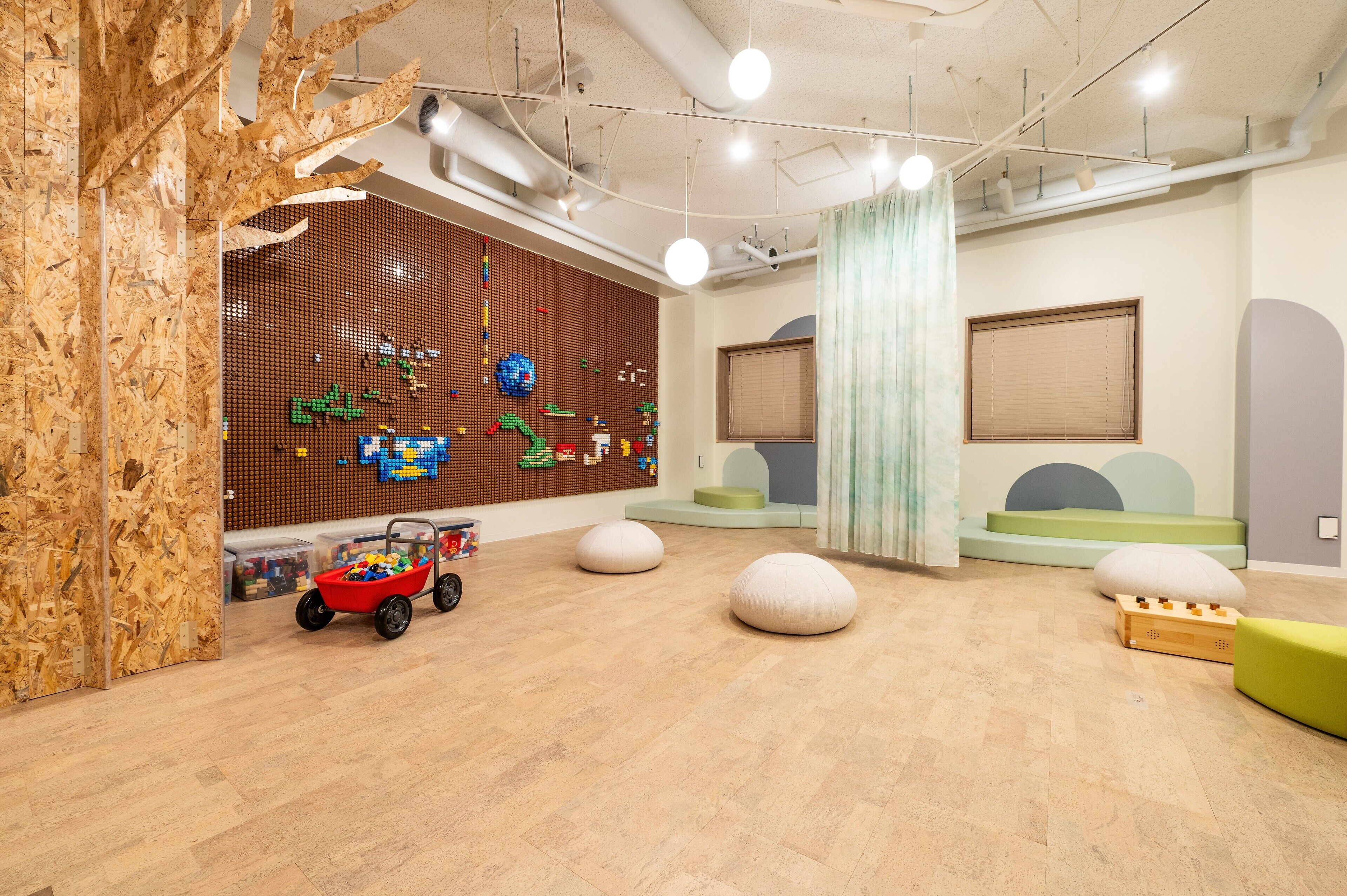 Un espace de jeux pour enfants comprenant une structure de jeu en bois, un mur décoré de motifs en pixel art colorés et plusieurs coins salon.