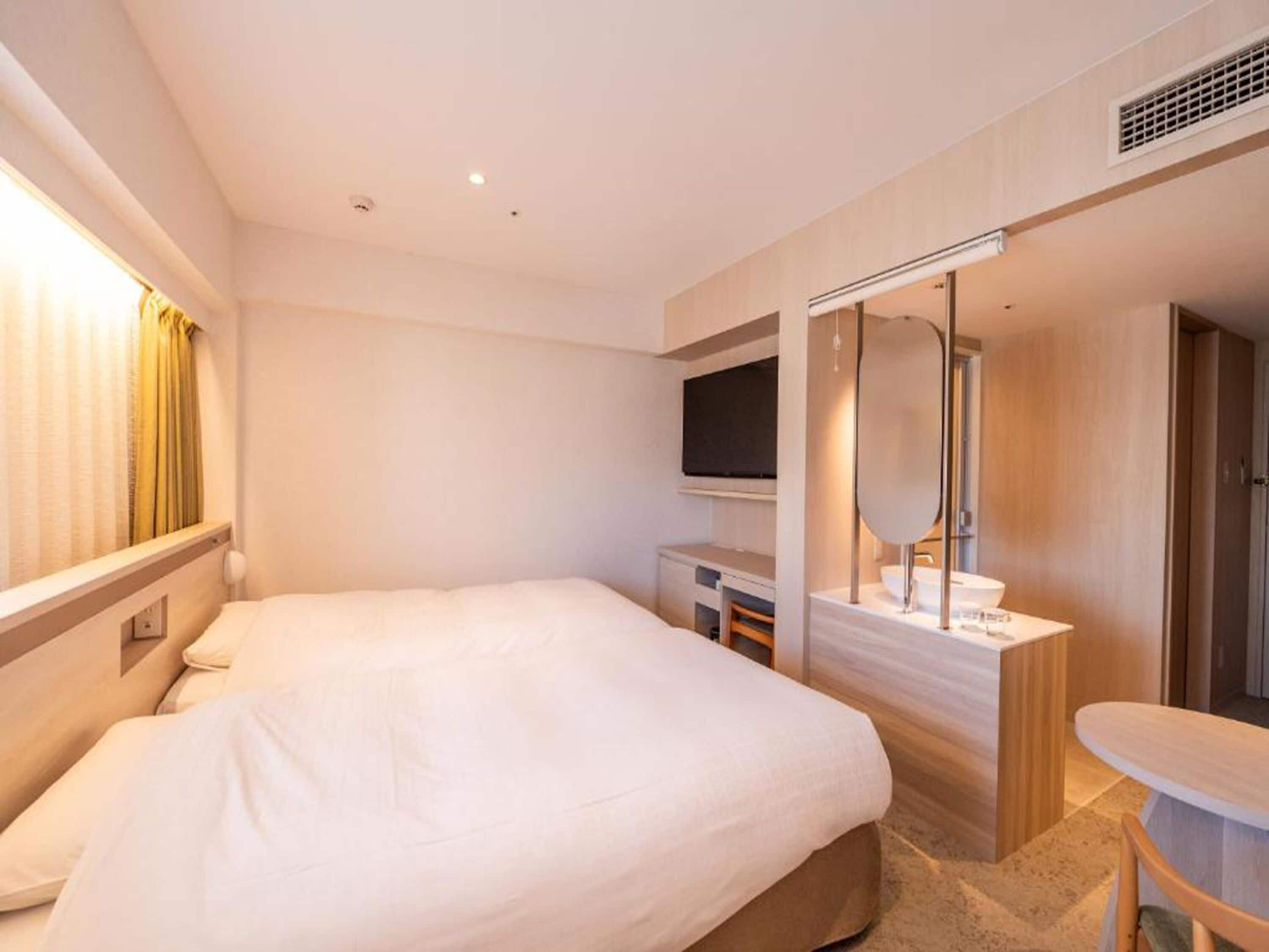 Une chambre d’hôtel moderne dotée d’un grand lit, d’un bureau avec un téléviseur à écran plat, d’une coiffeuse avec un miroir et d’une petite table.