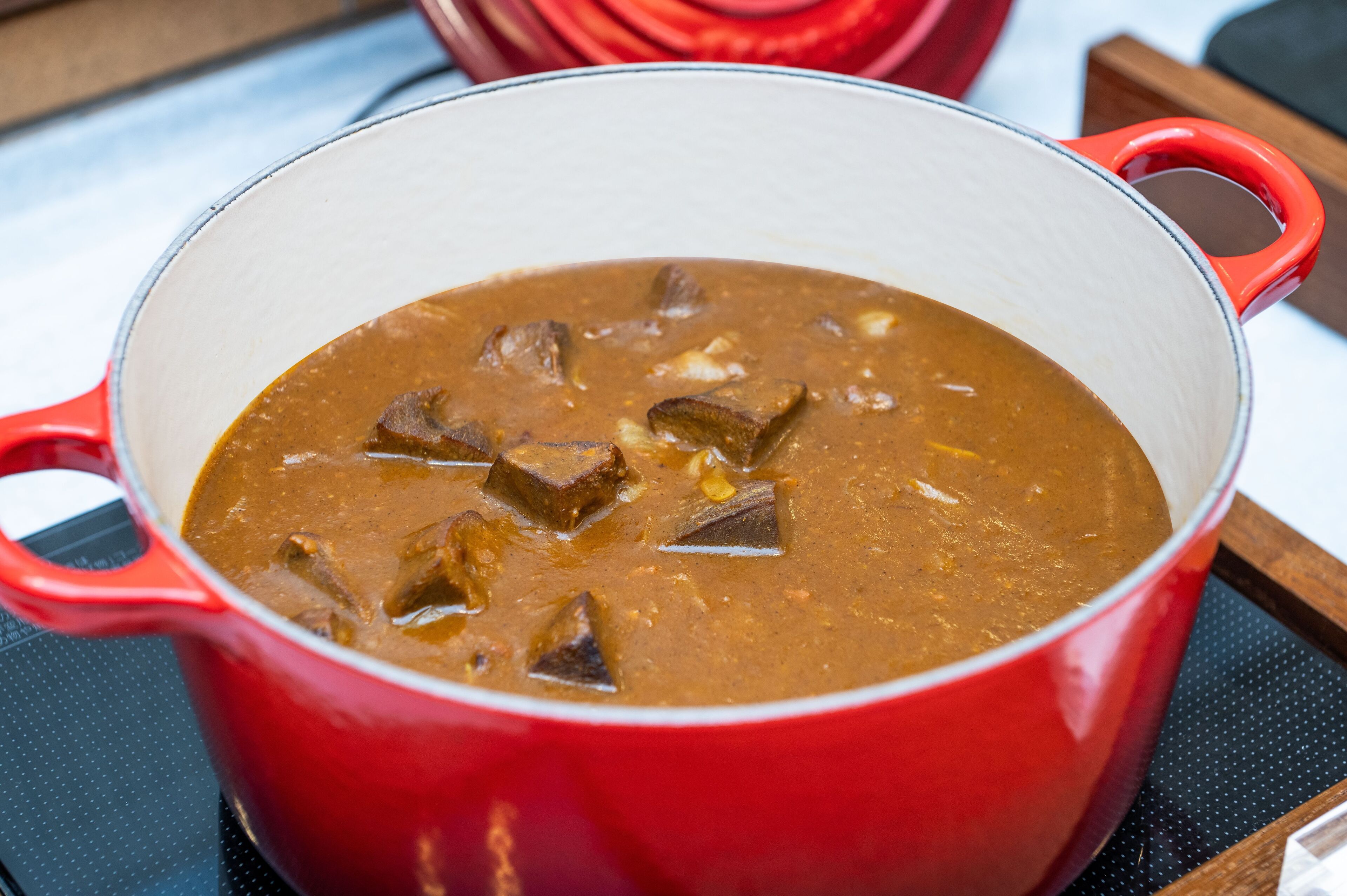 A red pot with a white interior containing a brown soup with chunks.