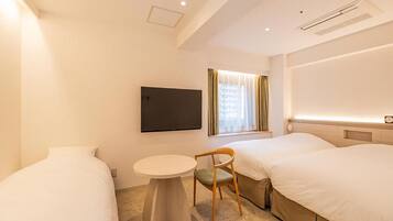 Quarto de hotel com duas camas, uma mesa redonda pequena, uma cadeira, uma televisão na parede e uma janela com cortinas.