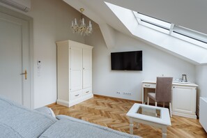 A room with a herringbone wooden floor, a white wardrobe, a television mounted on the wall, a desk with a chair, and a small table. - High Heaven Residence (Prague)