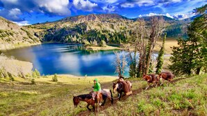 A person riding a horse along a dirt path with a lake and mountains in the background. - Buffalo Valley Ranch (Moran)