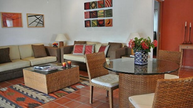 Una sala de estar con un sofá, dos sillones, una mesita de centro y una mesa de comedor con cubierta de vidrio.