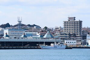 A coastal cityscape with a large white ship docked at a pier, a bridge, and various buildings including a tall structure with red signage. - Sun Marine Kesennuma Hotel Kanyo (Kesennuma)