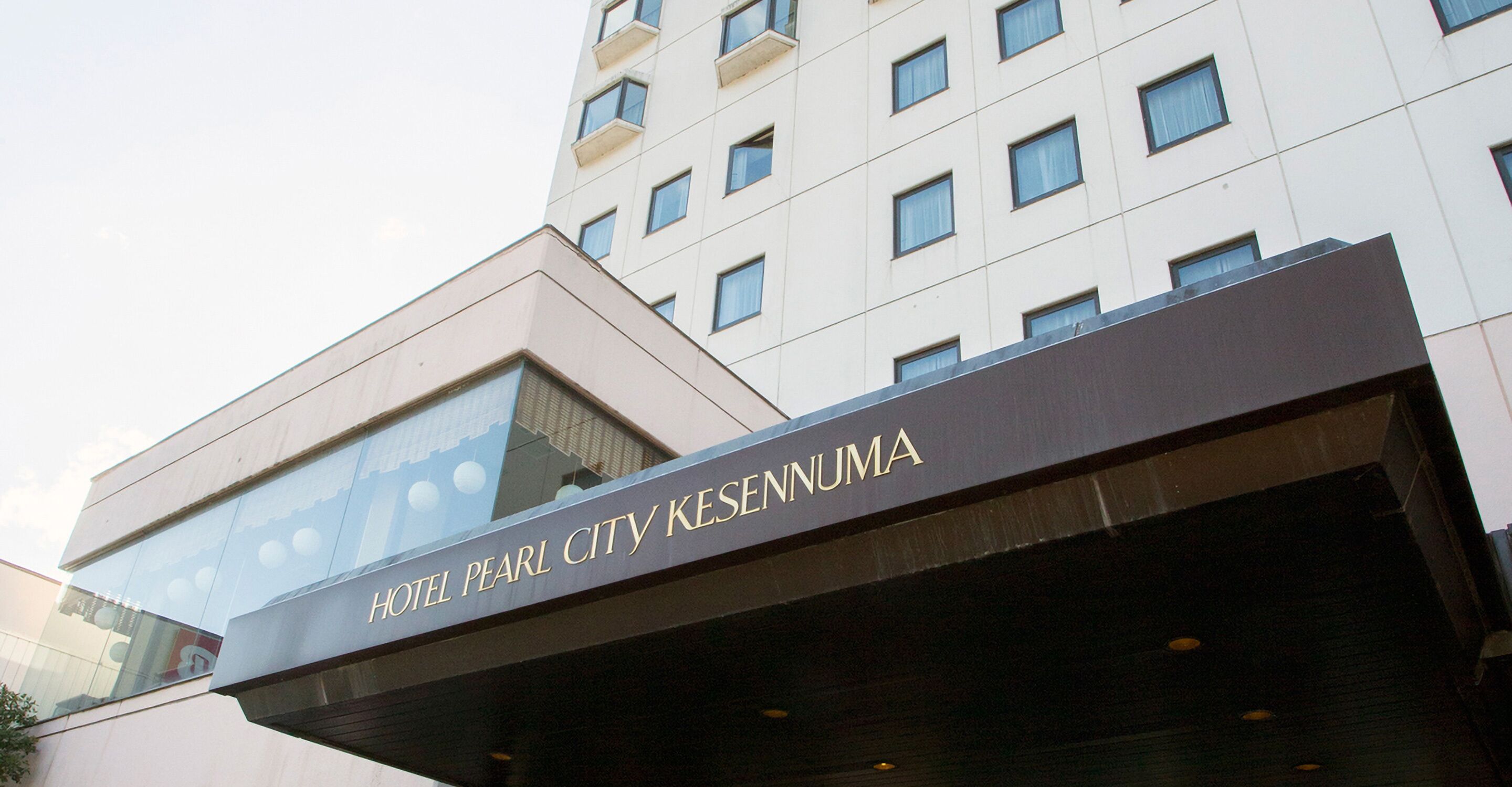 Exterior del Hotel Pearl City Kesennuma, con un diseño arquitectónico moderno que destaca una entrada imponente y amplias ventanas.