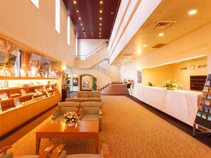 A hotel lobby with a reception desk, seating area, and a staircase leading to an upper level.