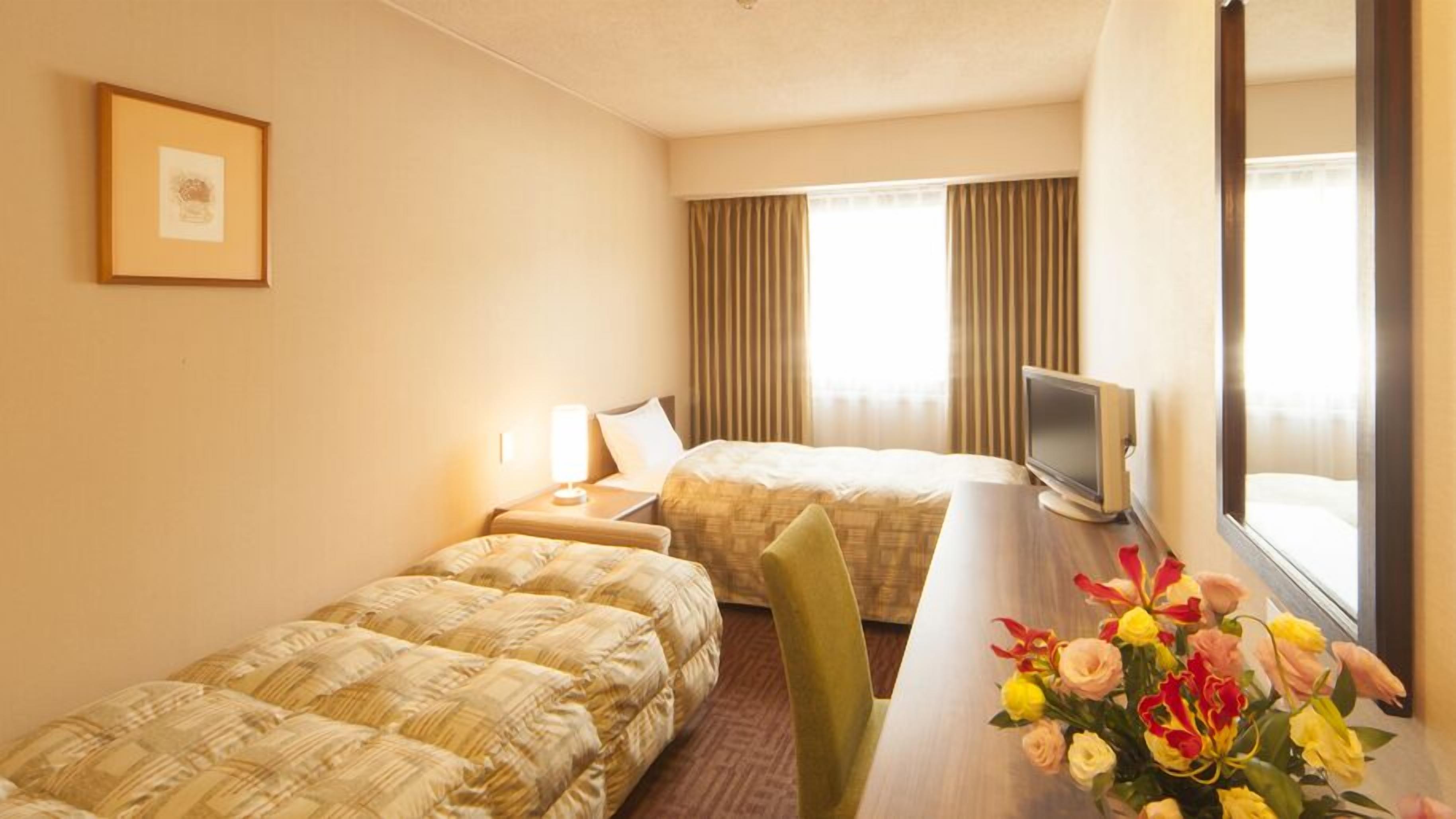 A hotel room with two beds, a desk with a TV, a framed picture on the wall, and a window with curtains.