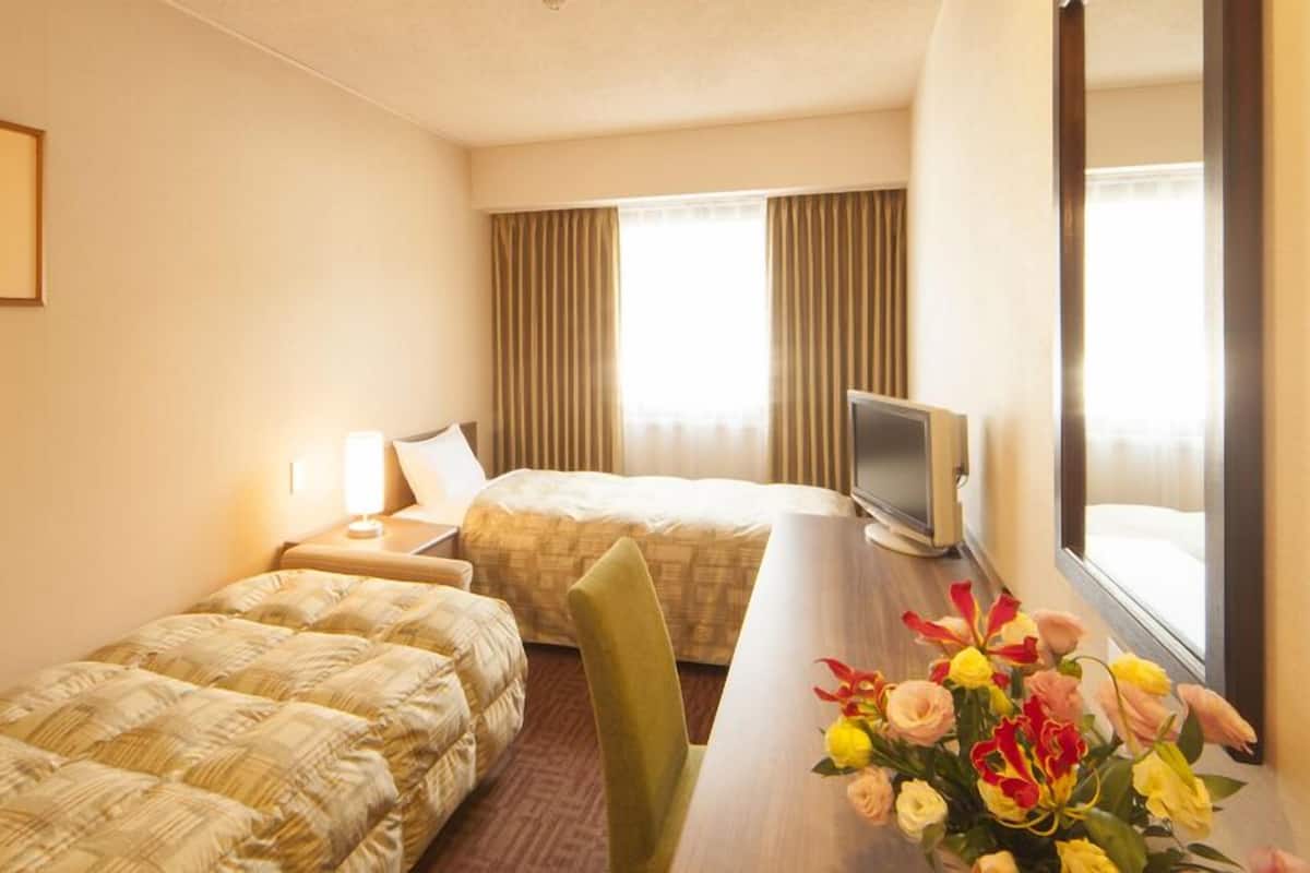 A hotel room with two beds, a desk with a TV, a framed picture on the wall, and a window with curtains.