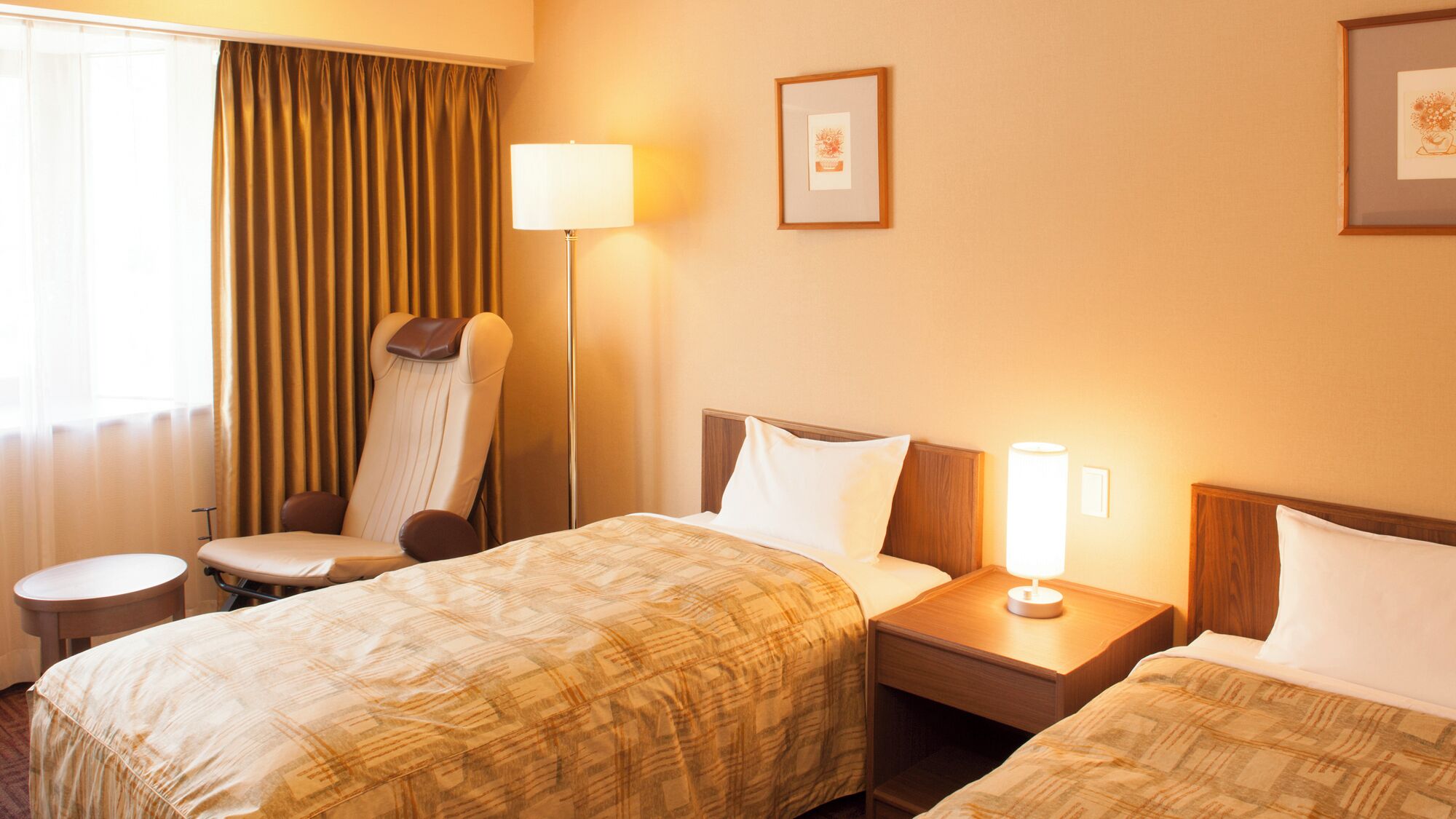 A hotel room with two beds, a chair, a bedside table, a lamp, and curtains.