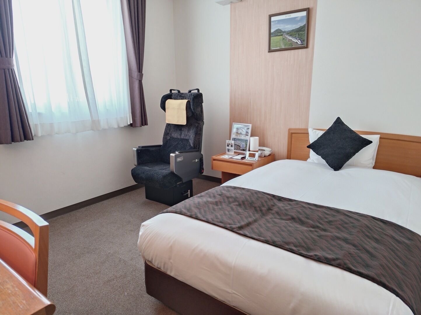 A hotel room with a bed, a chair, a nightstand, and a window with curtains.